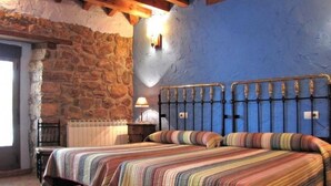 Un dormitori amb dos llits, parets de pedra, sostre de fusta i una paret blava.