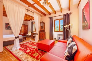 A room with a bed, a red sofa, a wooden ceiling, a large window, and a painting on the wall.