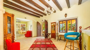 Un vaste espace de vie doté d’un plafond en bois, d’un fauteuil rouge, d’un tabouret de bar bleu et d’un tapis à motifs.