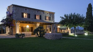 Une villa en pierre avec un toit en tuiles, une véranda et une pelouse bien entretenue.