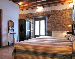 Ein Schlafzimmer mit einer Steinwand, einem Bett mit gestreifter Bettdecke, einer Holzbalkendecke und einer Tür mit Glasfeldern.