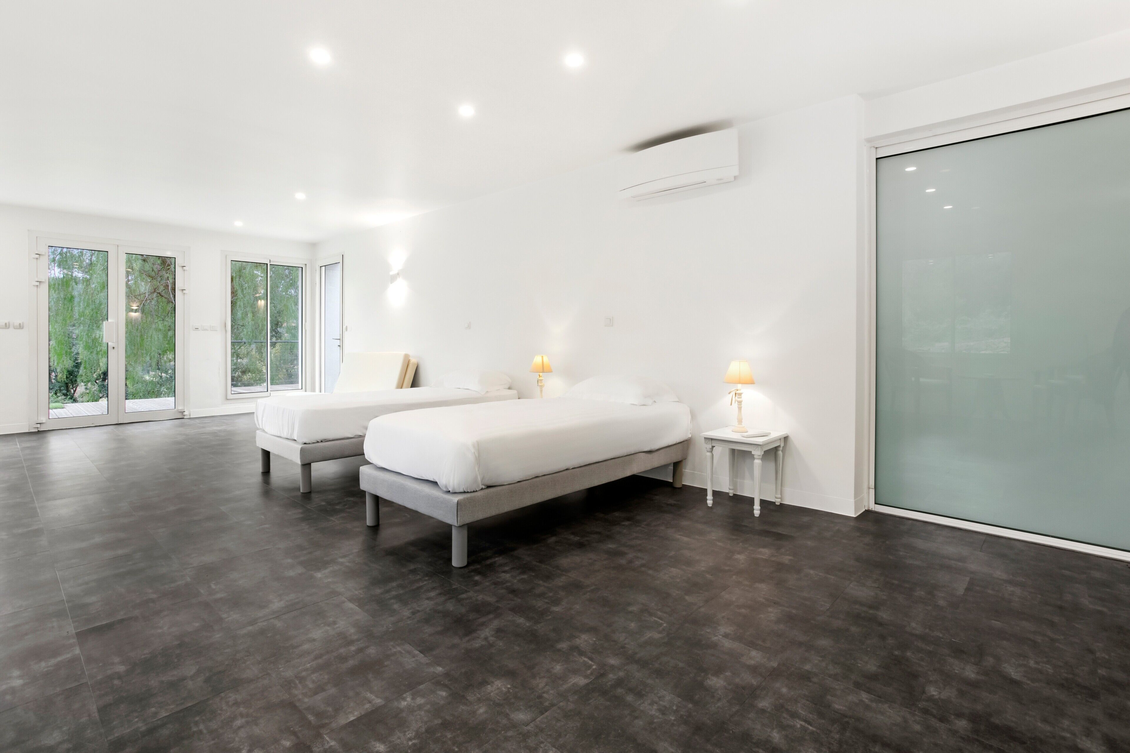 A modern bedroom with two beds, a large sliding glass door, and a white wall.