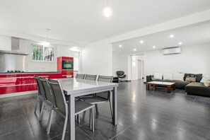 A modern kitchen with a red accent wall, a dining area with a white table and chairs, and a living area with a sofa and coffee table. - Villa "Stypa" with Private Pool, Wi-Fi and Air Conditioning (Trans-en-Provence)
