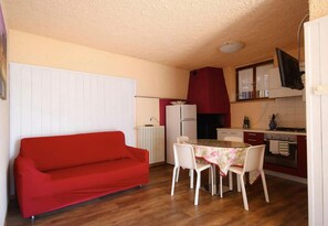 A compact kitchen with a dining table, chairs, a red sofa, and a white radiator.