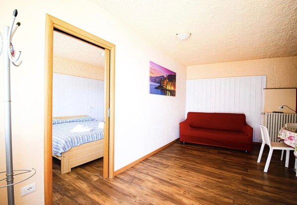 A room with a bed, a red sofa, a chair, a radiator, and a picture on the wall.