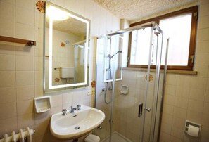 A bathroom with a sink, mirror, shower, and a window.