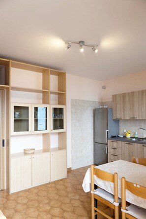 A compact kitchen with a refrigerator, wooden cabinets, and a dining table with chairs.