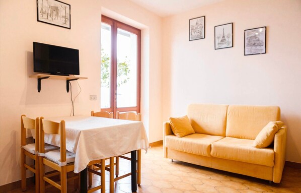 A room with a television mounted on the wall, a table with chairs, a sofa, and framed pictures on the wall.