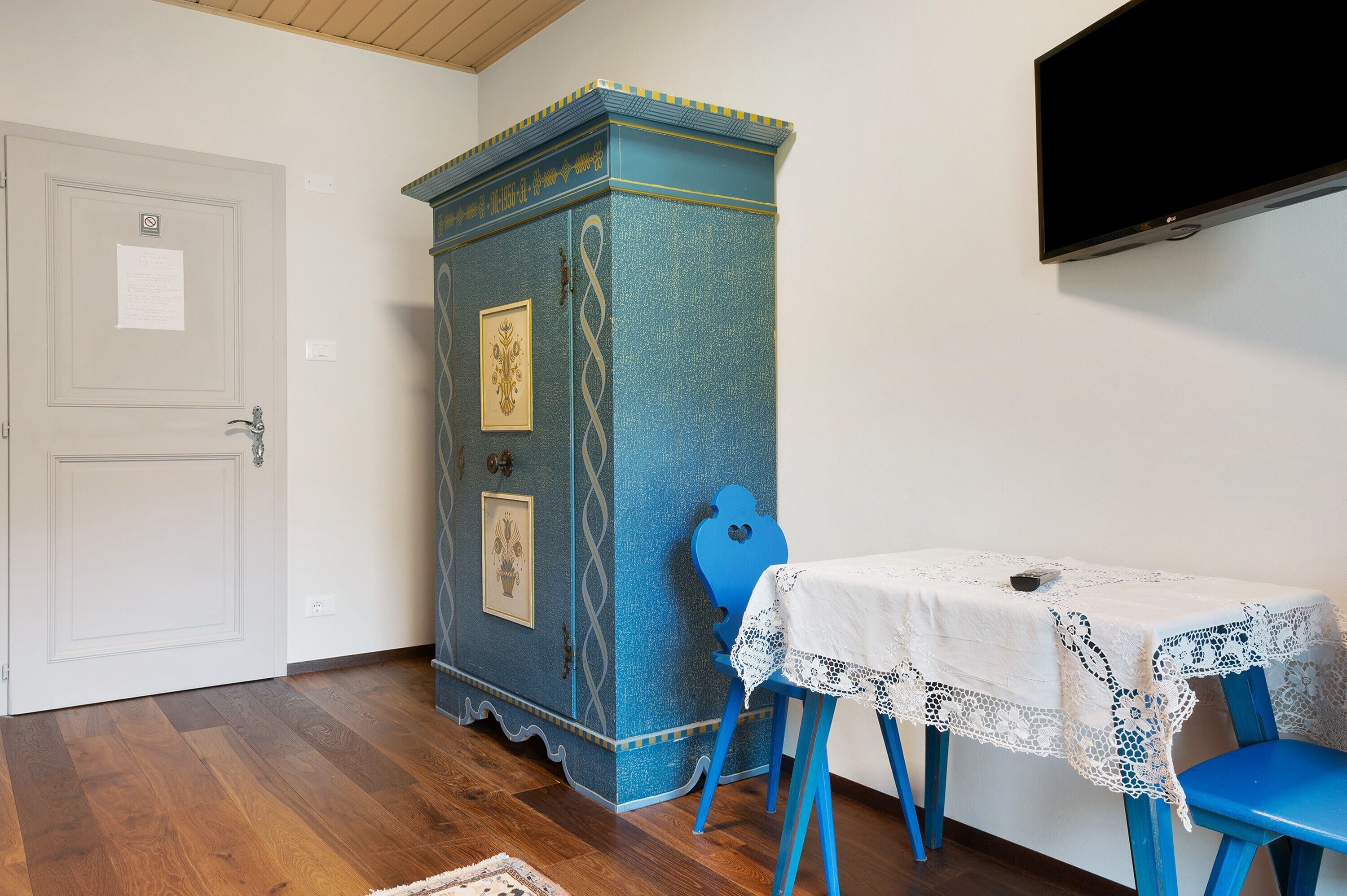 A room with a white door, a blue cabinet with decorative patterns, a table with a lace tablecloth, and blue chairs.