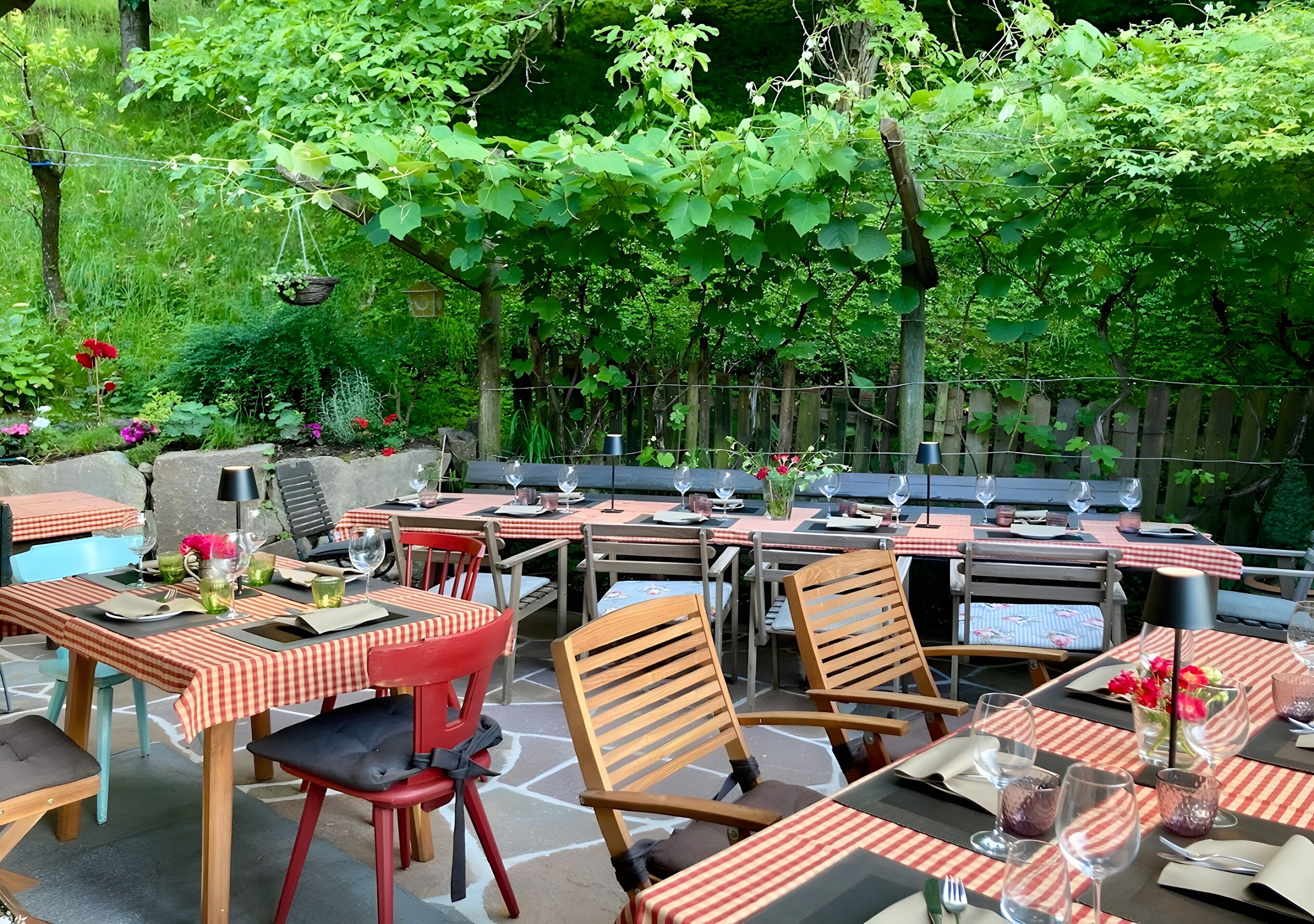 Une terrasse extérieure avec des tables et des chaises, entourée de verdure et d’une clôture en bois.