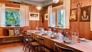 Comedor de madera con una larga mesa dispuesta para una comida, cuadros en las paredes y un banco con cojines.