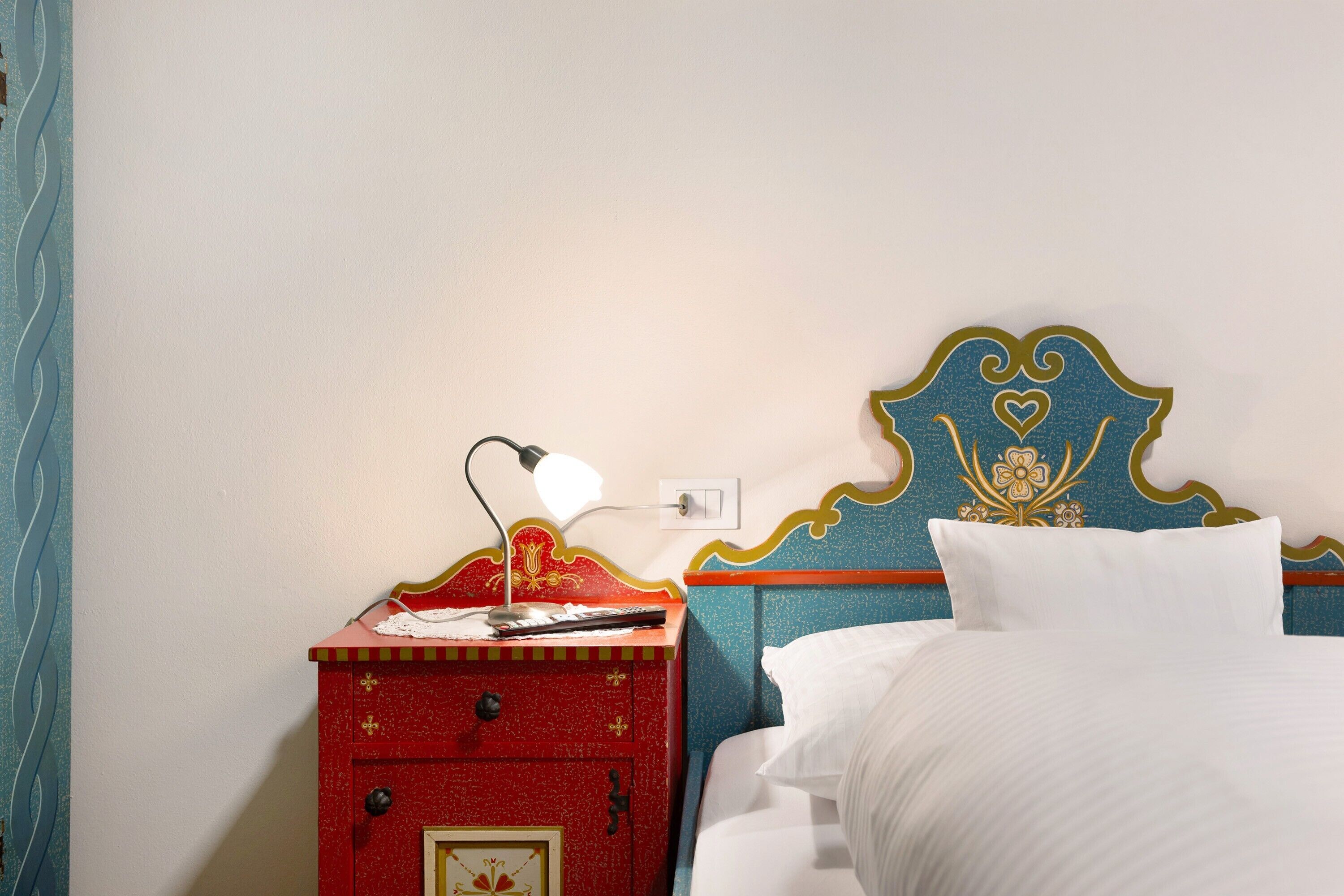 A bed with white bedding, a red nightstand with a lamp, and a decorative headboard.