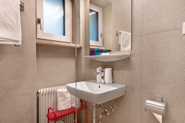 Un baño con un lavamanos blanco, un espejo, un perchero y una silla roja.