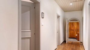 Un pasillo con piso de madera, paredes blancas y una puerta de madera al final.