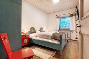 Une chambre à coucher avec un lit, une chaise rouge, une table de chevet, une fenêtre avec des rideaux et un radiateur.