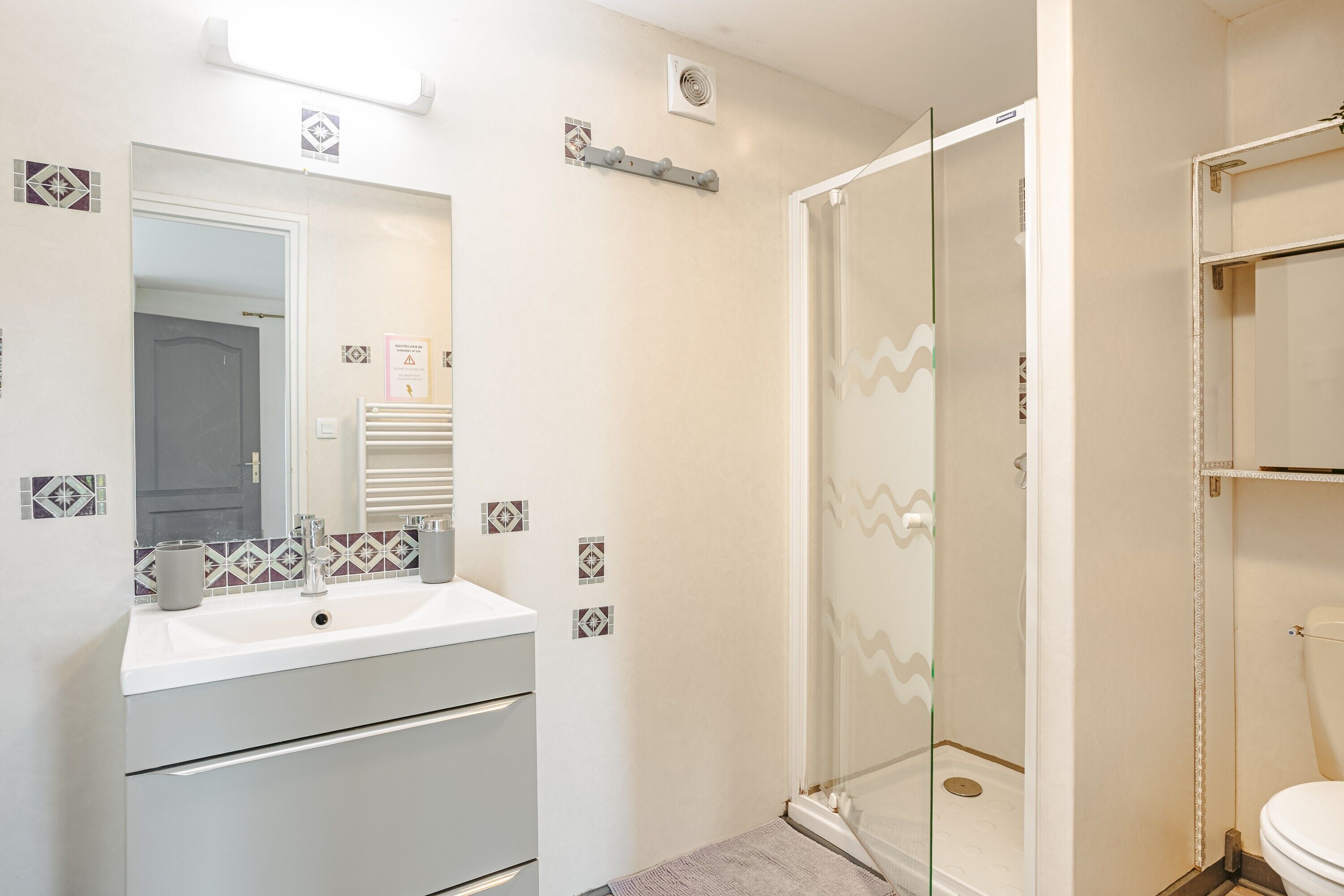 Een badkamer met een wit wastafelmeubel, spiegel en douche.