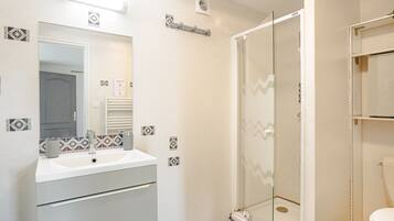 Een badkamer met een wit wastafelmeubel, spiegel en douche.