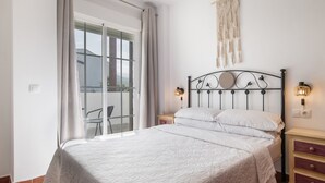 Une chambre à coucher avec un lit, des tables de chevet, une décoration murale en macramé et une vue accessible par une porte coulissante.