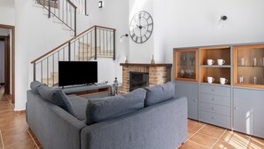 Un salon moderne avec un canapé gris, un téléviseur à écran plat, une cheminée, un escalier et un meuble en bois doté de portes en verre.