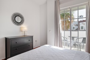 A bedroom with a bed, a dresser, a mirror, a window with curtains, and a view of the outside.