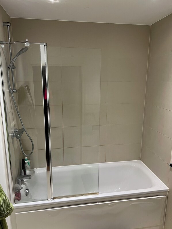 A bathroom with a glass-enclosed shower, a white bathtub, and beige tiled walls.