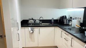 A modern kitchen with white cabinets, a black countertop, and a wooden floor.