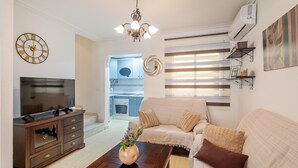 Een woonkamer met een televisie, een houten kast, een bank, een bijzettafeltje en een kroonluchter.