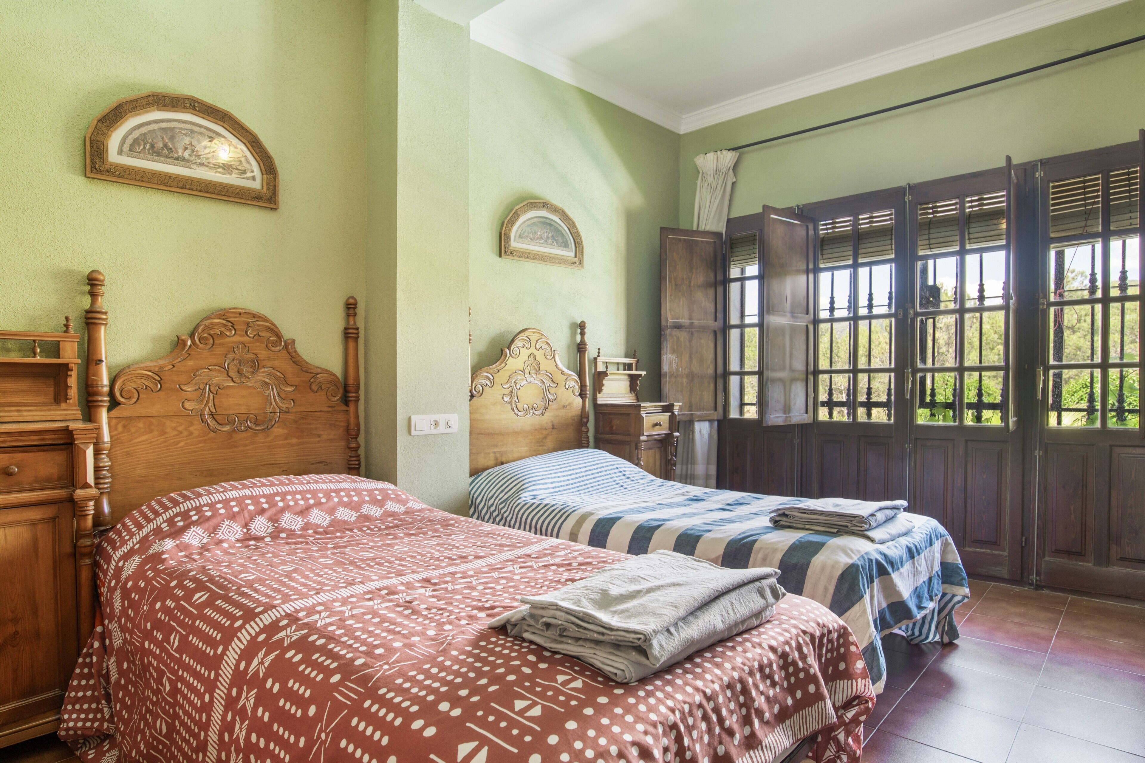 A room with two beds, a wooden dresser, and a window with a view of greenery.