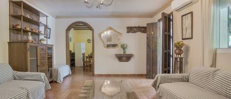 A living room with a glass coffee table, two striped sofas, a wooden cabinet, and a chandelier.
