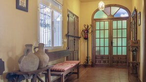 Un couloir avec un banc, deux grands vases, un extincteur et une porte en bois dotée de panneaux de verre.