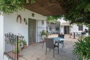 A patio with a table and chairs, potted plants, a metal gate, and a building in the background.