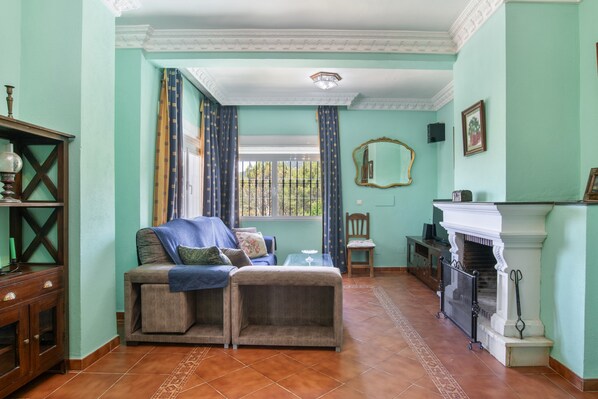 A room with a sofa, a fireplace, a window with curtains, a mirror, and a wooden cabinet.