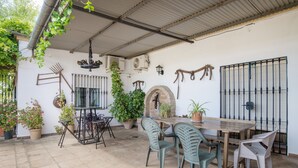 Une terrasse extérieure avec une table et des chaises, entourée de plantes en pot et d’un mur de briques rustiques.