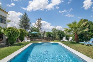A rectangular swimming pool with a patterned edge, surrounded by a grassy area and trees.