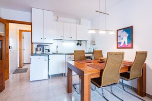A compact kitchen with white cabinets, a dining table with chairs, and a small refrigerator.