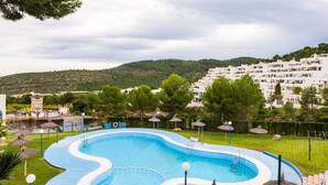 Une piscine à bord ondulé, entourée d’une clôture, avec une pelouse et des arbres en arrière-plan.