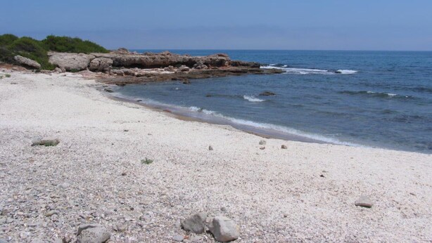 Une plage de galets avec un promontoire rocheux et une mer calme.