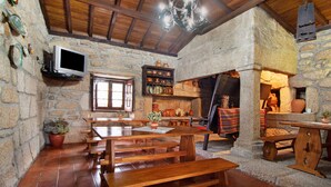 Un interior rústico de piedra con bancos de madera, una chimenea y un televisor montado en la pared.