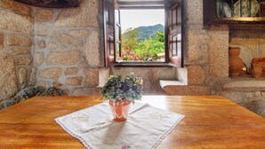 Un muro de piedra con una ventana, una mesa de madera con un mantel y una planta en maceta.
