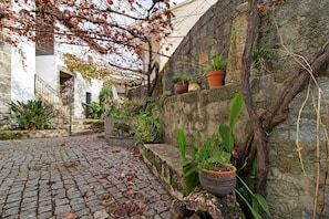 A cobblestone courtyard with stone walls, potted plants, and a staircase leading to an upper level.