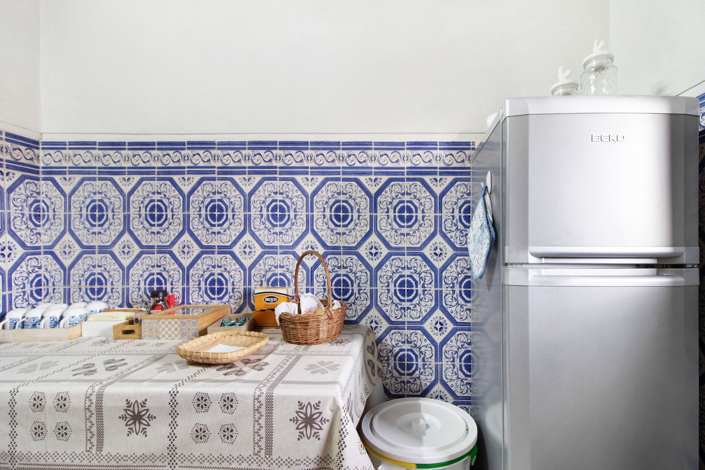 A kitchen with a patterned backsplash, a refrigerator, and a table with various items.