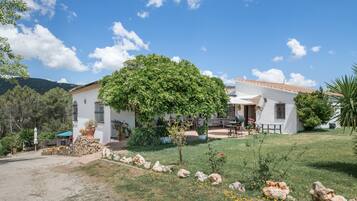 A white building with a tiled roof, a garden with rocks and plants, and a clear blue sky.