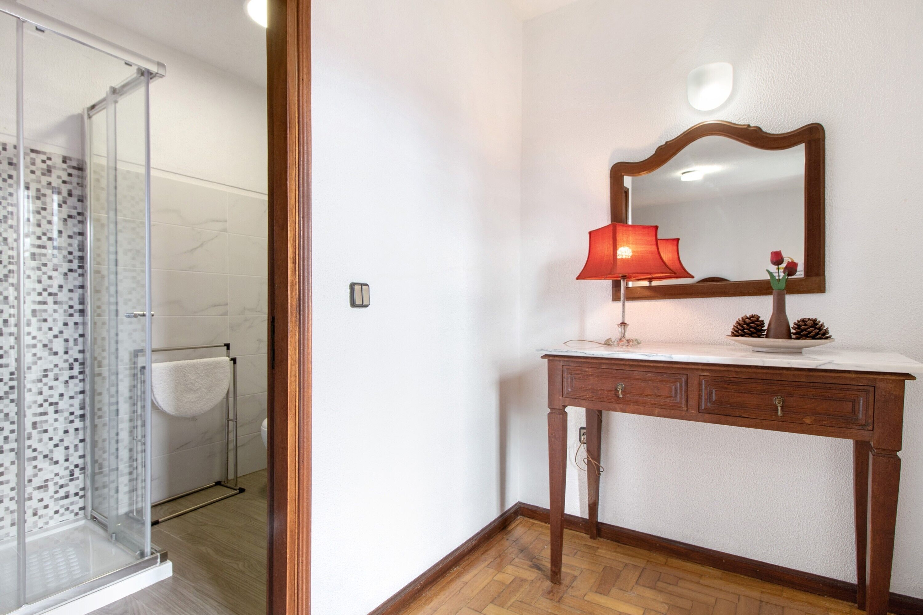 Un baño con cabina de ducha de vidrio, tocador de madera con espejo y una lámpara roja.
