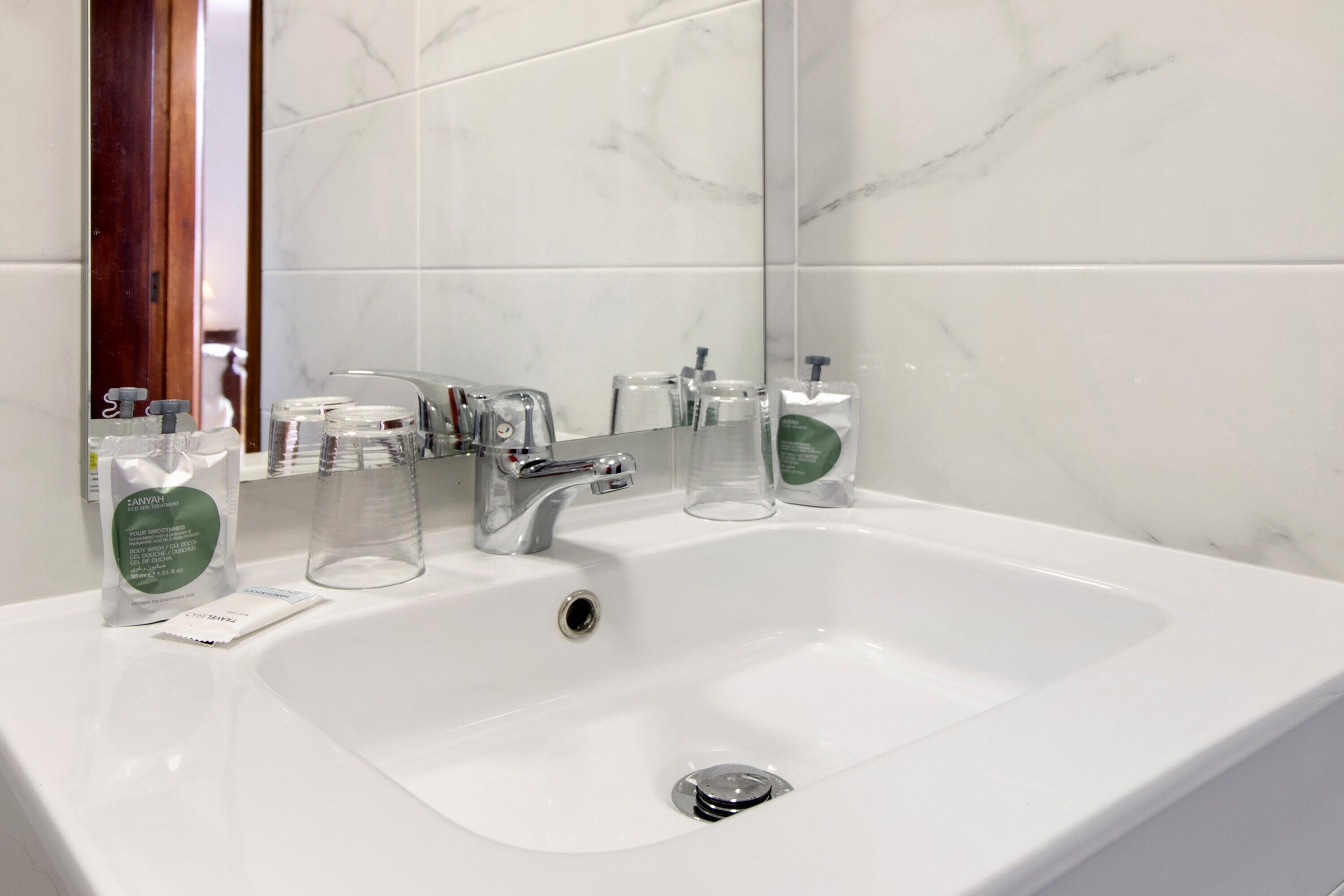 Un lavabo blanc pour la salle de bain, avec un miroir, un robinet chromé et deux distributeurs de savon en verre transparent.