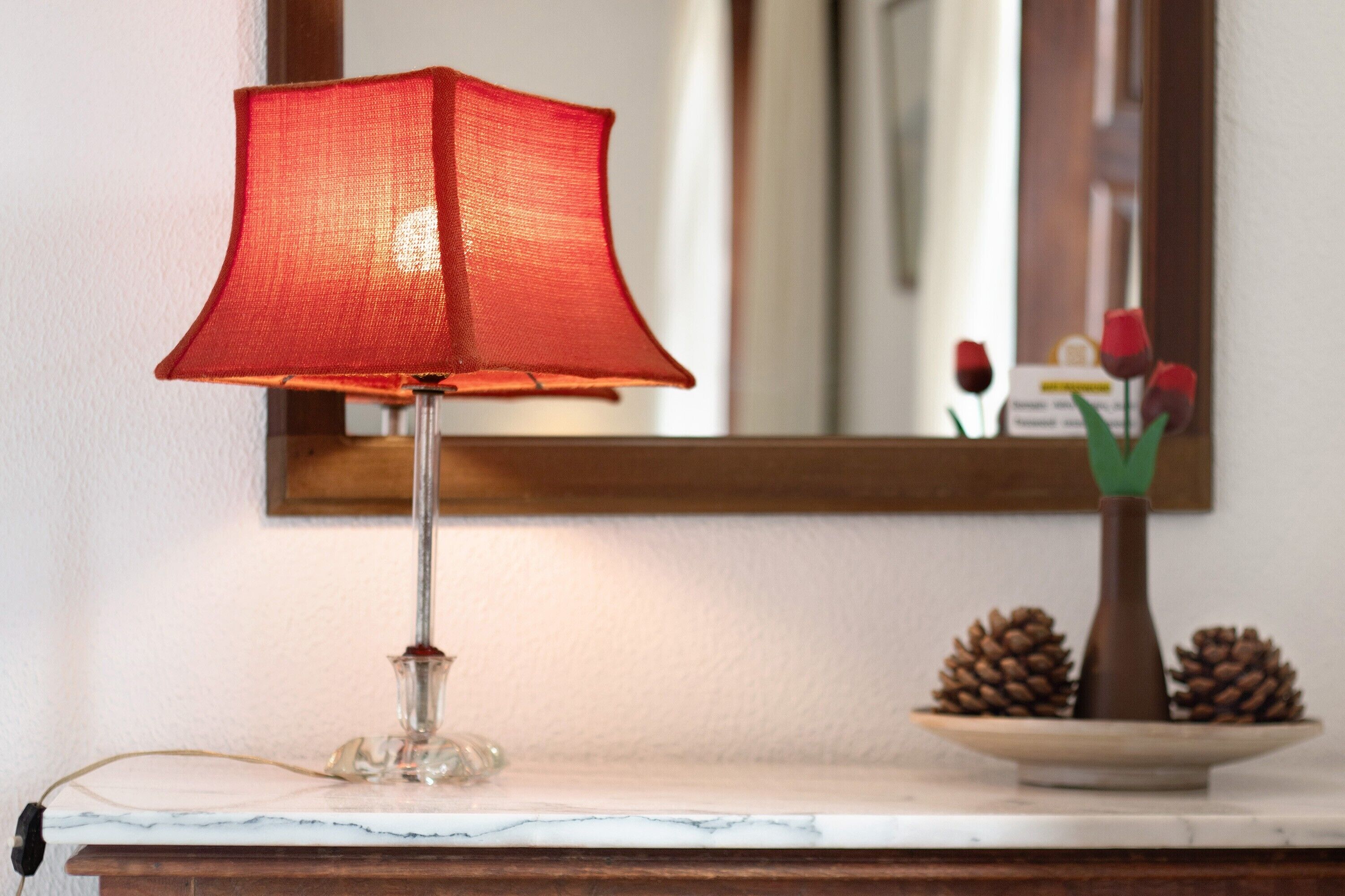 Une lampe posée sur une surface en marbre, avec un miroir qui reflète des fleurs et des pommes de pin.