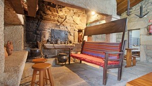 Una habitación rústica con paredes de piedra, un banco de madera, taburetes y una chimenea.
