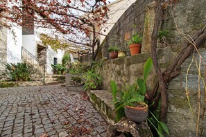 Un cortile lastricato con pareti in pietra, piante in vaso e una scala che conduce a un piano superiore.