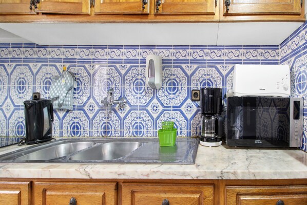 A kitchen with a sink, a coffee maker, a microwave, and a green dish rack.