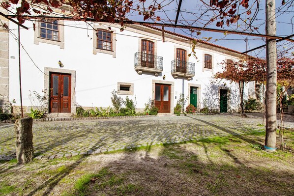 A white building with multiple doors and windows, a cobblestone courtyard, and a tree with bare branches.