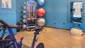 Une salle de sport équipée de matériel d’exercice, notamment un vélo d’appartement, un porte-balles et un téléviseur fixé au mur.